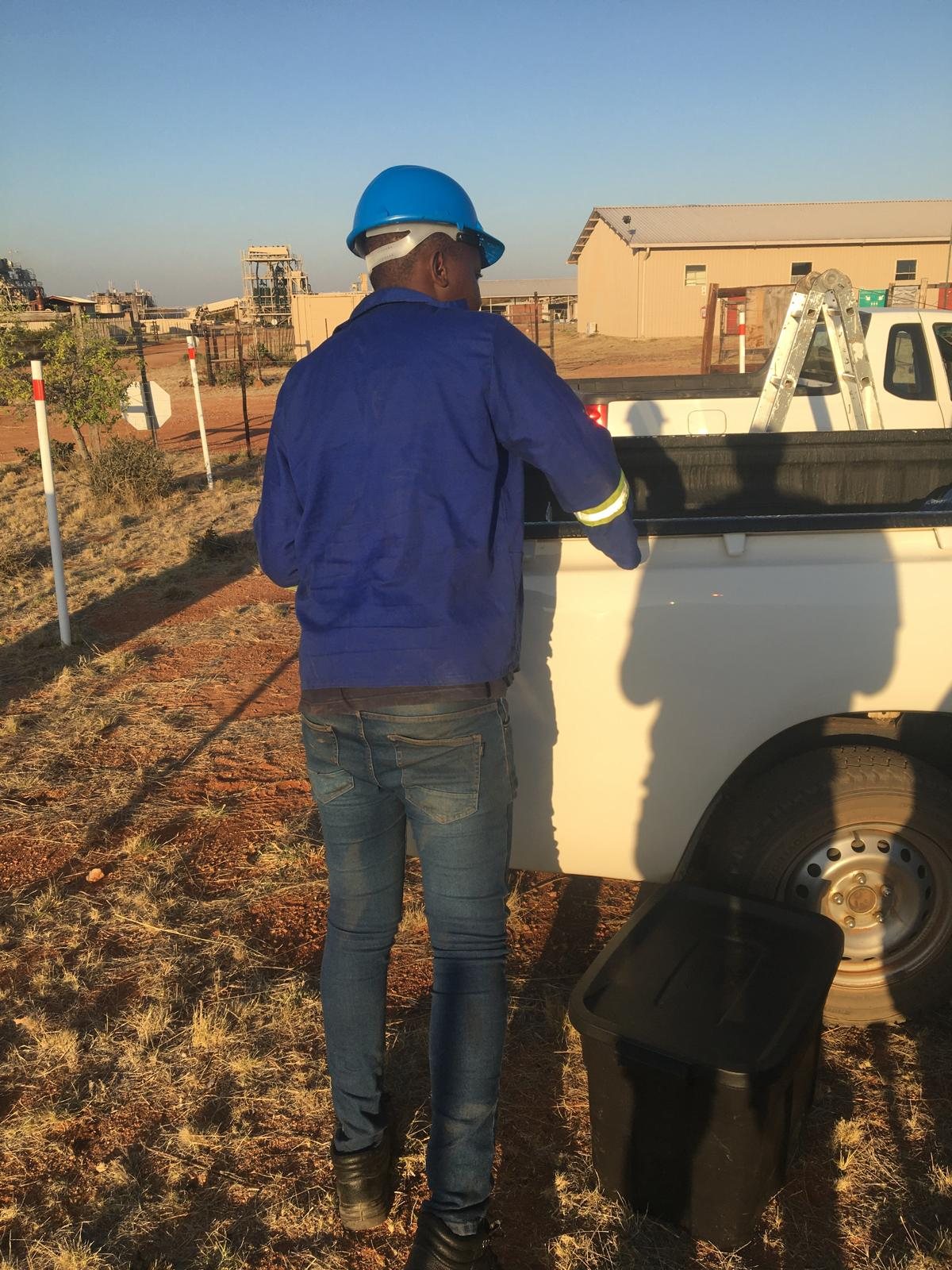 IT technician in a hard hat at an industrial site standing beside a service bakkie