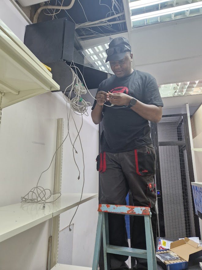 IT Guy Solutions technician on a ladder terminating network cables into a ceiling cabinet