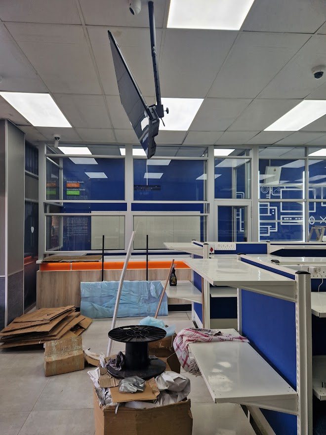 Branch interior during IT fit-out with a ceiling-mounted display, cabling and shopfitting in progress