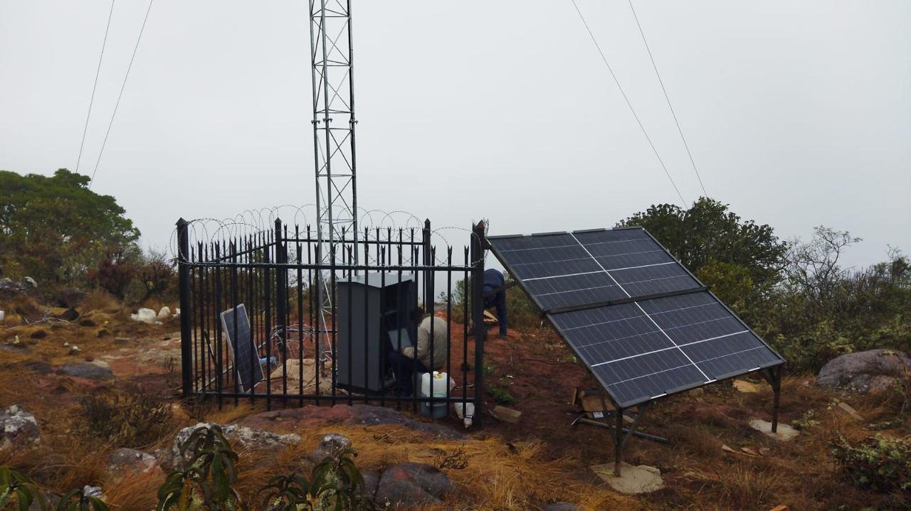 Fenced hilltop communications compound with a solar array, outdoor cabinet and lattice tower