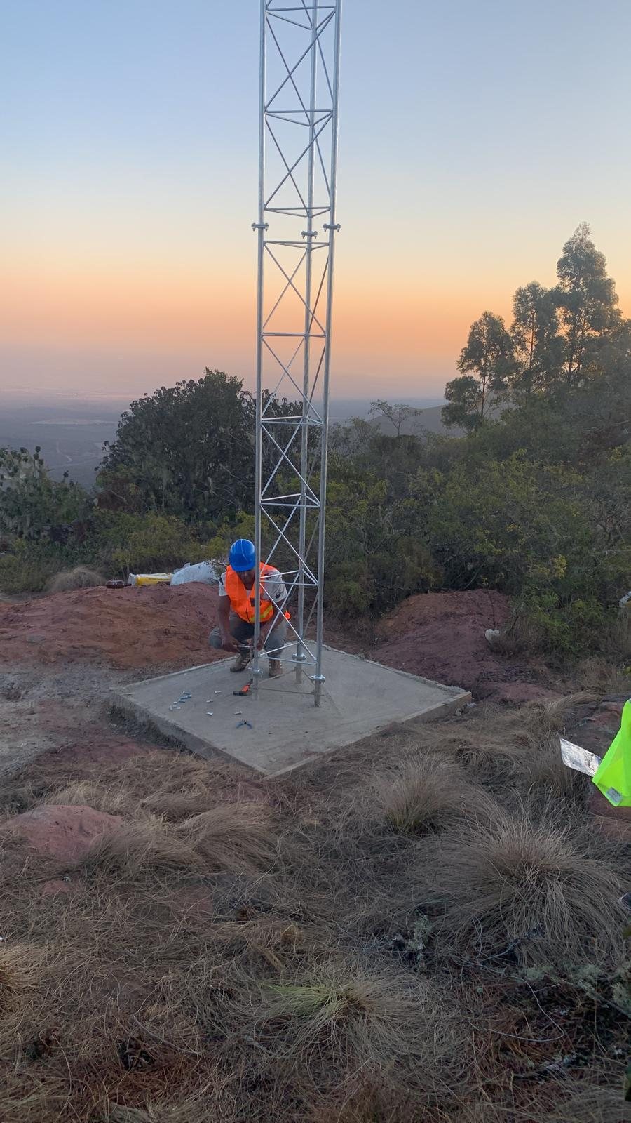 Technician assembling lattice tower sections on a Limpopo hillside at dusk