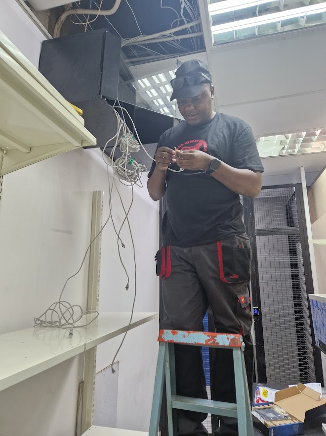 Technician on a ladder terminating network cabling into a ceiling-mounted cabinet