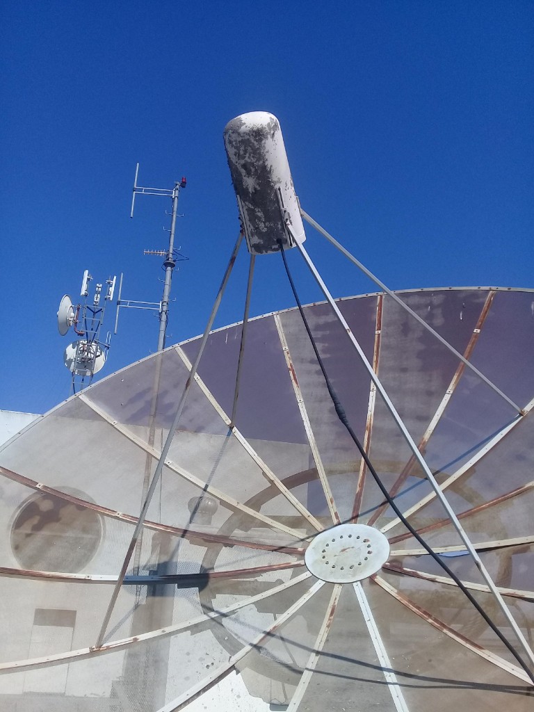 Mesh parabolic dish with feed horn on a rooftop next to other antennas
