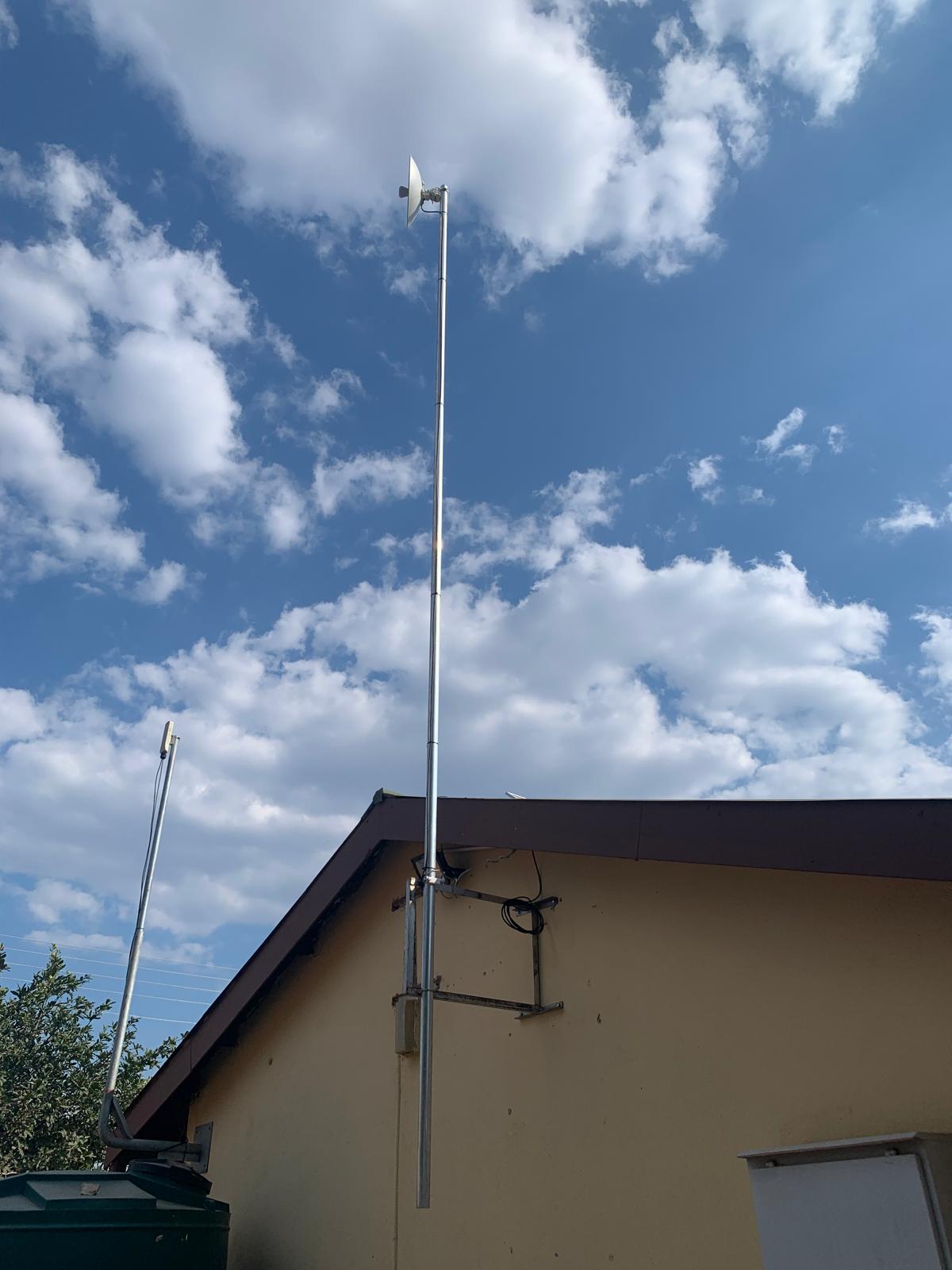 Tall building-mounted pole carrying a small wireless dish above a roof