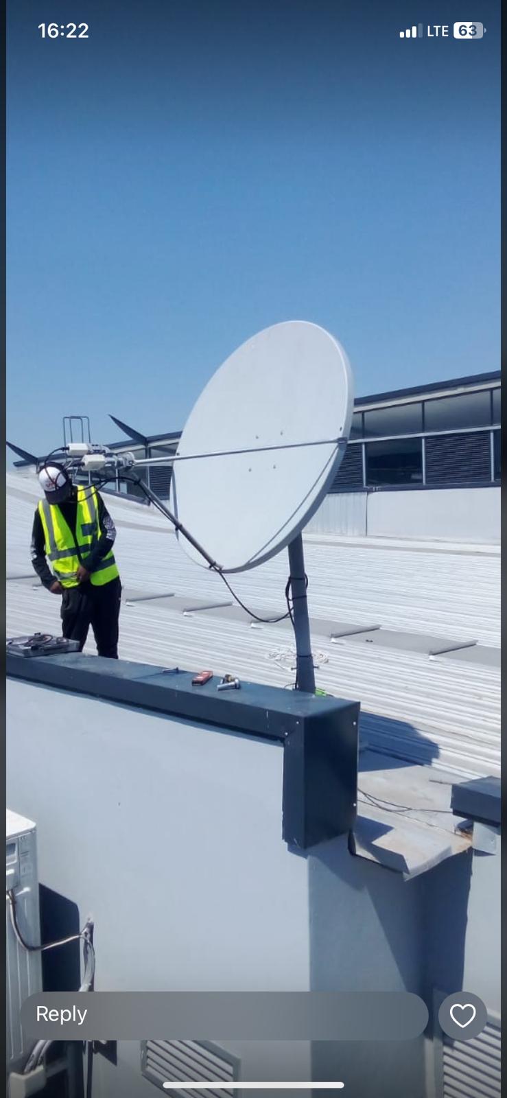 Technician in high-visibility clothing next to a satellite dish on a commercial metal roof