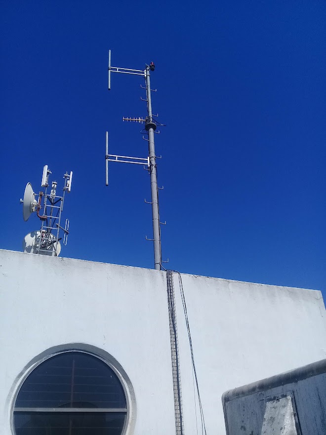 Building-mounted mast with yagi and panel antennas above a white parapet