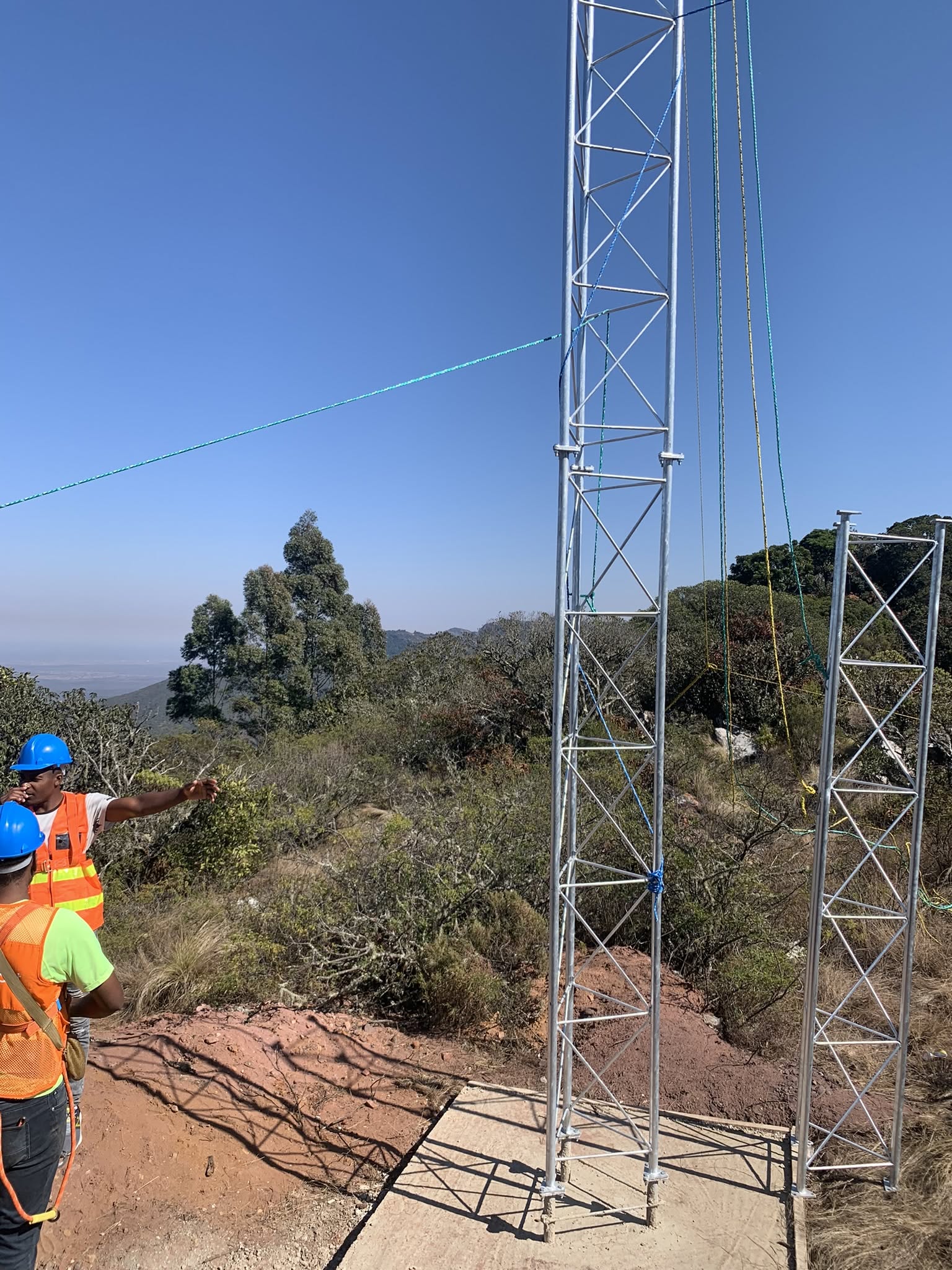 Crew assembling lattice tower sections on a hilltop pad with tag lines