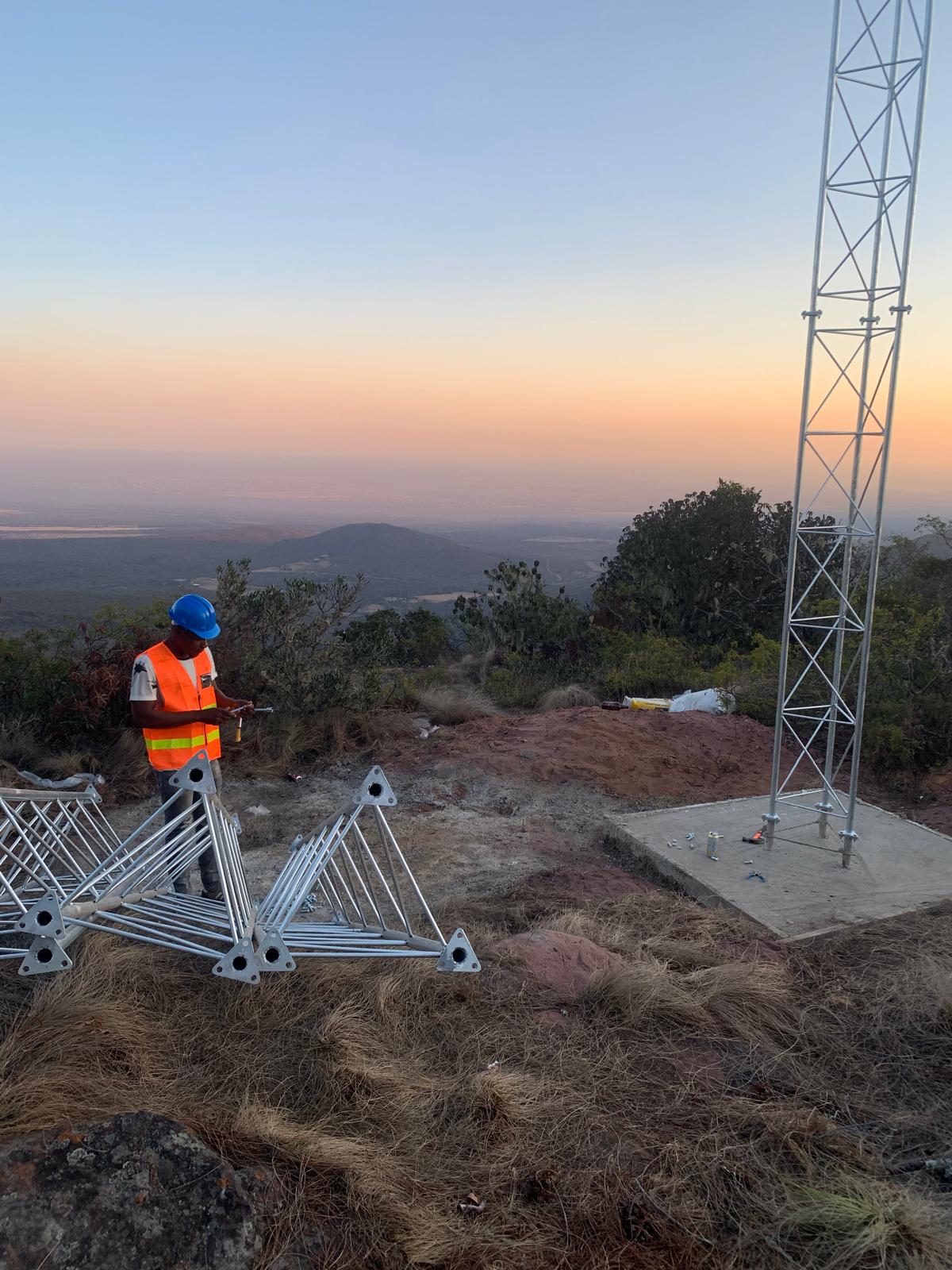 Two technicians climbing a lattice tower at dusk wearing helmets and harnesses